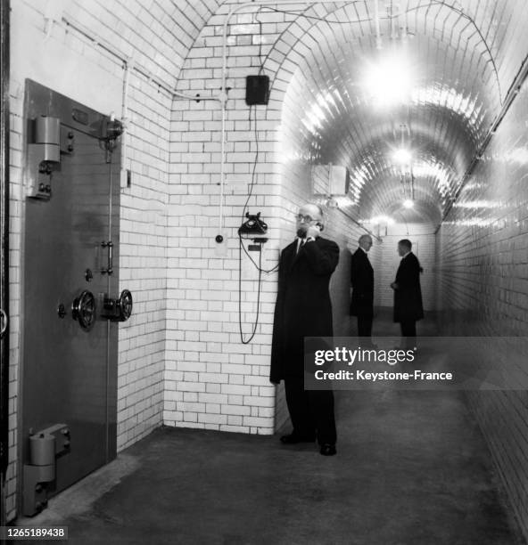 Intérieur d'une banque londonienne avec porte blindée pour accéder à la salle des coffre-forts, et le gardien au téléphone en juillet 1969 à Londres.