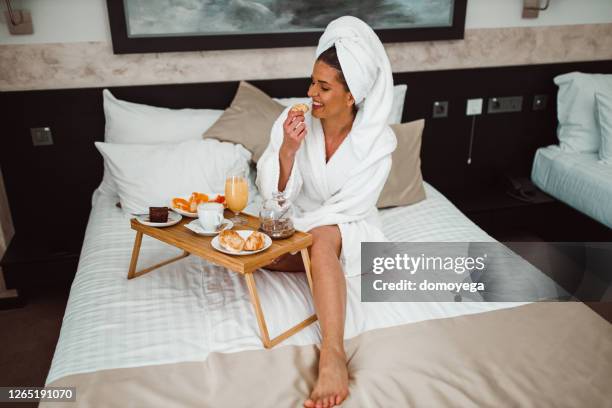 vrouw die een badjas draagt die ontbijt in bed eet - amenities hotel stockfoto's en -beelden