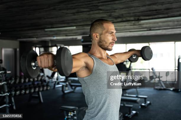 young handsome man doing exercises in gym shoulder workout with dumbbell fitness health club - on shoulders stock pictures, royalty-free photos & images