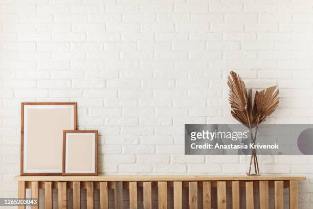 dry gold palm leaf in a glass vase and two pho frames standing on wood shelf. stylish trendy decoration on white background. - bohemian background stock pictures, royalty-free photos & images