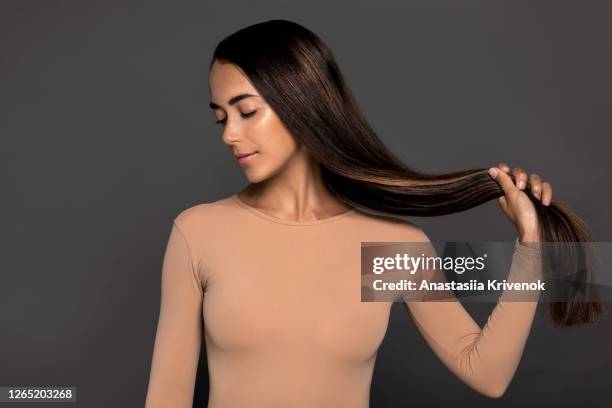 brunette girl with long straight and shiny hair. beauty skin woman holding her strong and healthy hair in her hands over grey background. cosmetic hair beauty salon concept. - long gray hair stock pictures, royalty-free photos & images