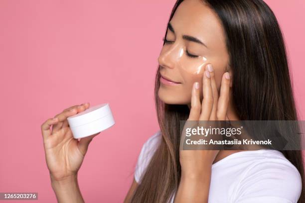 portrait of beautiful woman wears an eye patches and massage eye zone on pink background. 30s woman age holding container or jar of collagen eyes pads. advertising your product, copy space. - face mask beauty product - fotografias e filmes do acervo