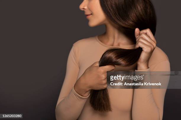 brunette girl with long straight and shiny hair. beauty skin woman holding her strong and healthy hair in her hands over grey background. cosmetic hair beauty salon concept. - langes haar stock-fotos und bilder
