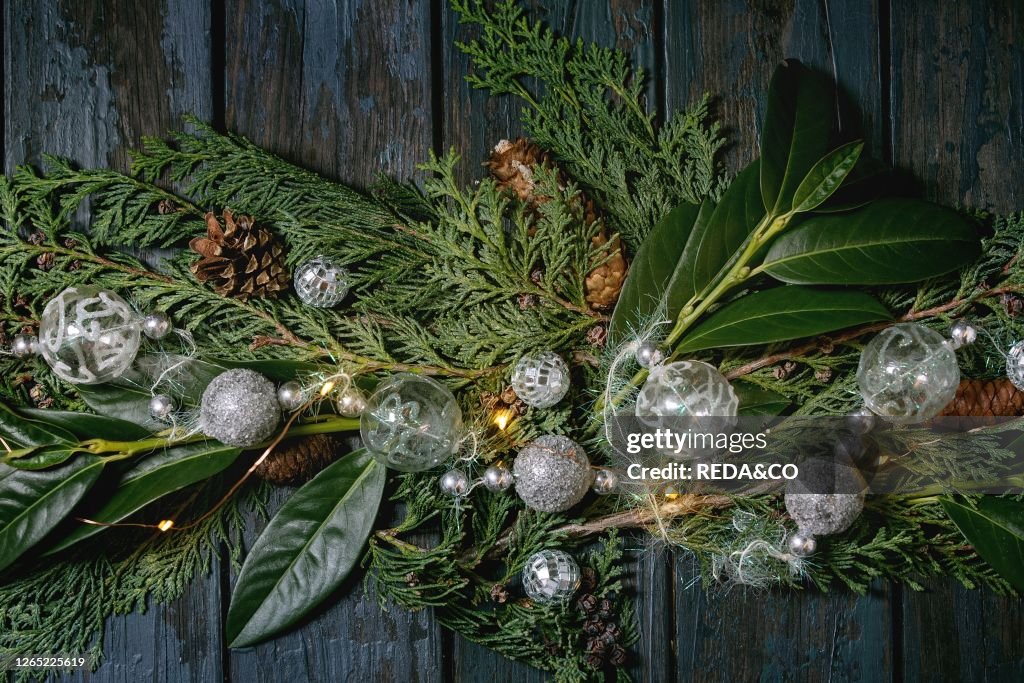 Green Christmas table decor thuja branches. leaves. silver balls and lighted garlands over dark blue wooden background. Flat lay. space. Christmas and New year decorations or greeting card.