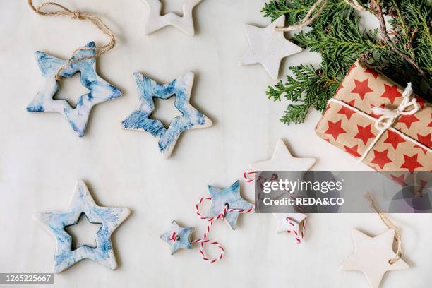 Christmas decoration ceramic stars white and blue glazed. Different size. Gift boxes in craft paper. Green branches over white marble background....