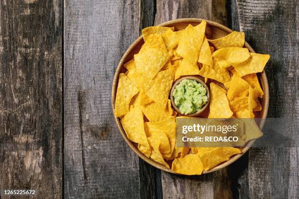 Tortilla nachos corn chips with avocado guacamole sauce served in wood plate over old wooden background. Flat lay. Space.