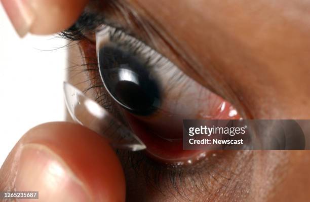 Facial close up of a young man putting a contact lens onto his eye..