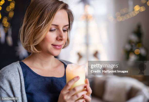 young woman with candle standing indoors at home at christmas time. - christmas candle stock pictures, royalty-free photos & images