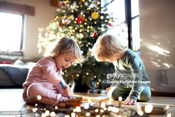 small children sitting indoors at home at christmas time, drawing pictures. - brother and sister stock-fotos und bilder
