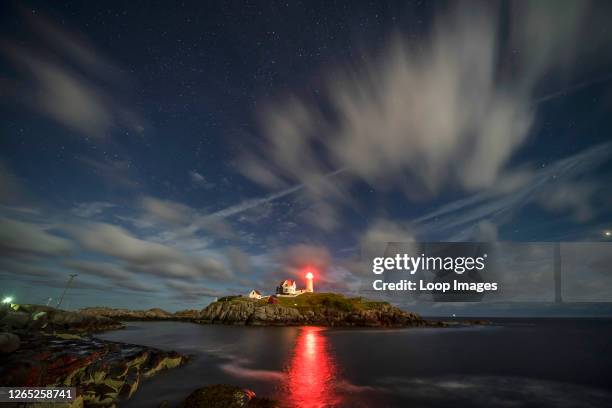 Starlit canopy and wisps of cloud pass over the Nubble Point Lighthouse along the Northeast coast of the United States.