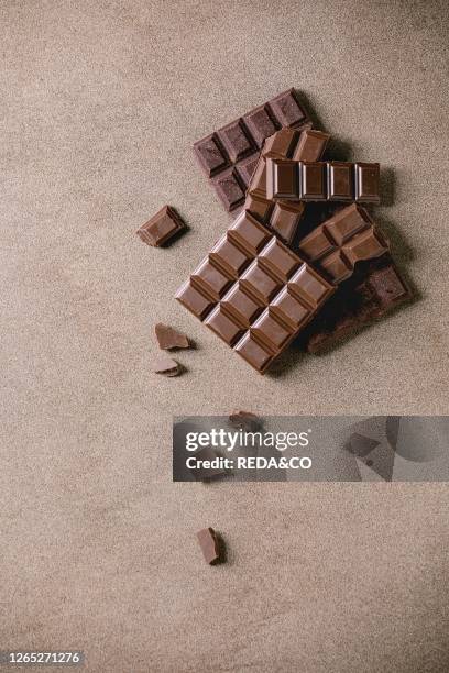 Dark and milk chocolate bar whole and chopped over brown texture background. Flat lay, space.