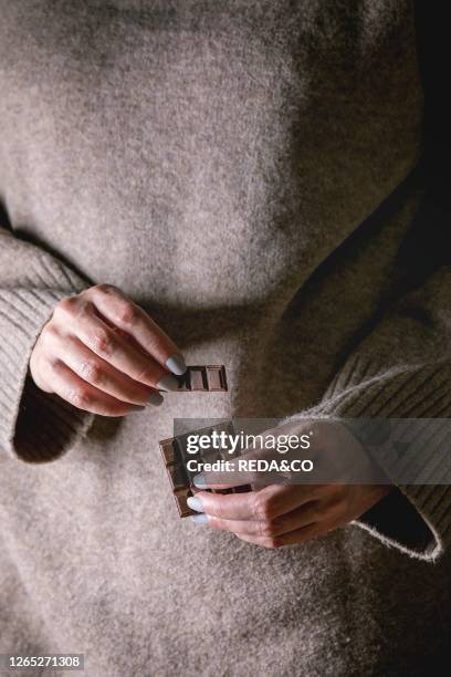 Woman beige sweater hold in hands broken dark chocolate bar.