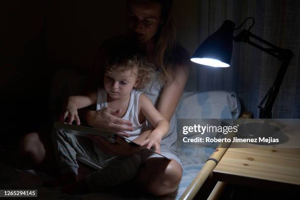 mother reading a book to her little boy at home in bed at night, - storytelling children stock pictures, royalty-free photos & images