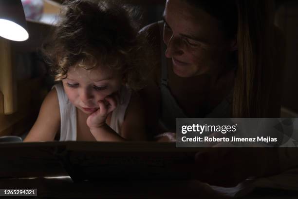 mother reading a book to her young son, lying in bed at night - storytelling children stock pictures, royalty-free photos & images