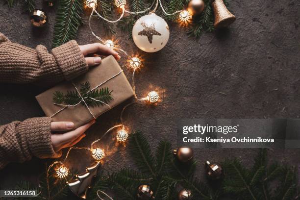 female hands holding christmas gift box on white wooden background with fir branches, pine cones. xmas and happy new year theme, bokeh, sparking, glowing. flat lay, top view - flatlay stock-fotos und bilder