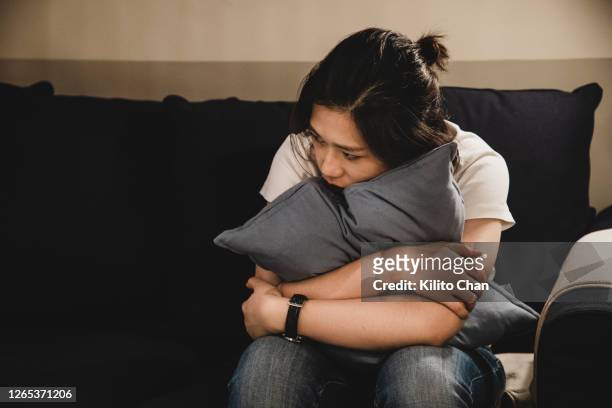 depressed asian woman sitting on sofa holding a cushion - hysteria fotografías e imágenes de stock