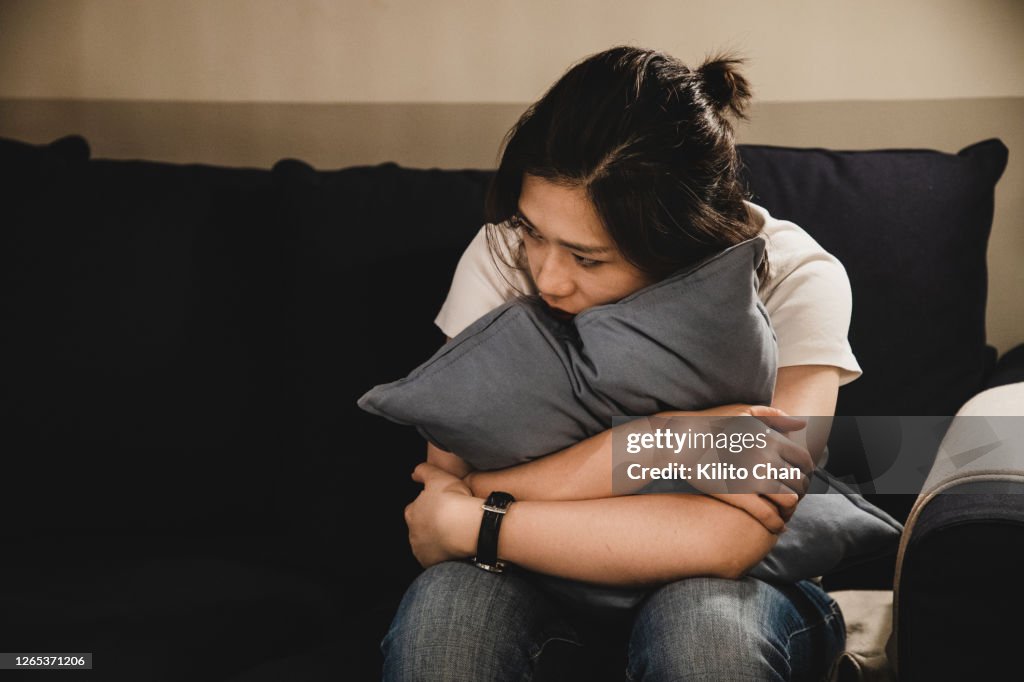 Depressed asian woman sitting on sofa holding a cushion