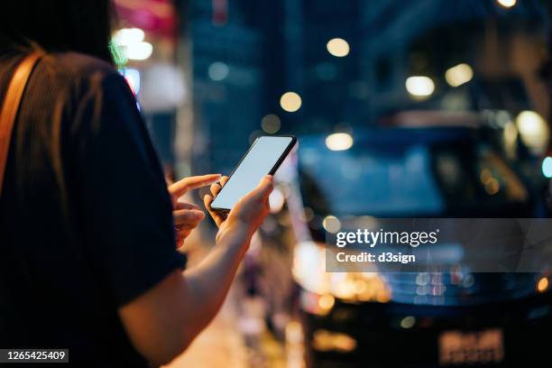 close up of young asian woman using mobile app device on smartphone to hail a taxi ride on city street after work in the evening - uber　ライドシェア ストックフォトと画像