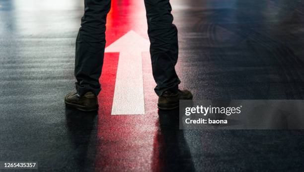 pieds d’homme d’affaires et flèche de direction sur le plancher. - marquage de route photos et images de collection