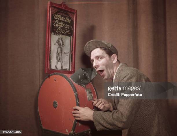 English actor and comedian Norman Wisdom operates a mutoscope motion picture device on the set of a television show in England in April 1952.