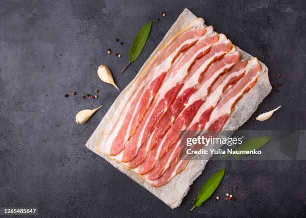 raw sliced bacon ready for cooking on dark black concrete background. ingredients of bacon, seasoning and herbs. prosciutto ready to eat. - jambon de parme photos et images de collection