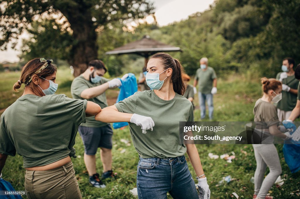 Grupo de voluntarios con máscaras quirúrgicas limpiando la naturaleza juntos