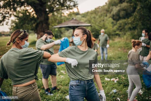gruppo di volontari con maschere chirurgiche che puliscono la natura insieme - esprimere a gesti foto e immagini stock