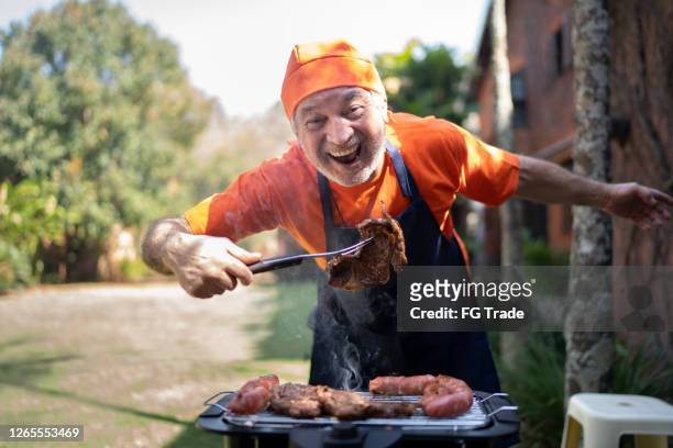 portrait of a happy senior man preparing a barbecue - fun experience stock pictures, royalty-free photos & images