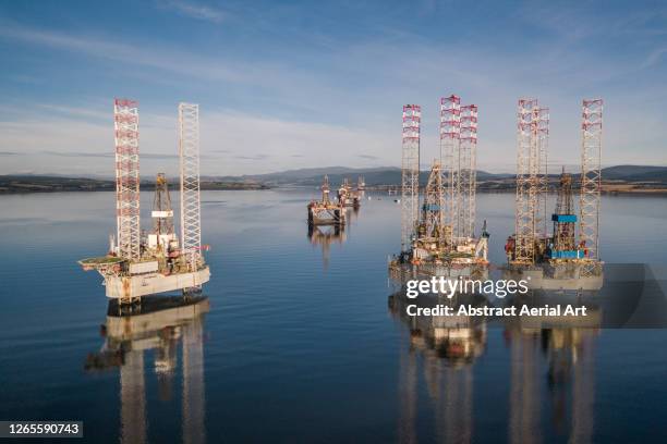 low angle drone shot showing the reflections of various oil drilling rigs in a calm ocean channel, cromarty firth, scotland, united kingdom - oil rig uk stock pictures, royalty-free photos & images