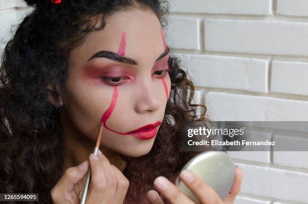 woman putting on evil clown makeup for halloween - geschminkt gezicht stockfoto's en -beelden