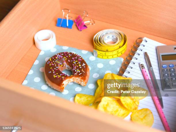 doughnut and potato chips in office desk - bulimie stock-fotos und bilder