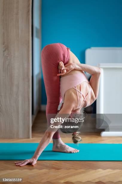 woman practicing yoga in uttanasana with one leg bent in front - flexibility stock pictures, royalty-free photos & images