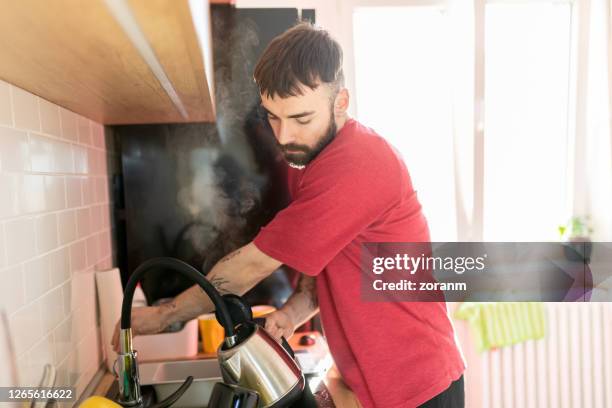 young man pouring water from faucet in the sink into kettle - kettle steam stock pictures, royalty-free photos & images