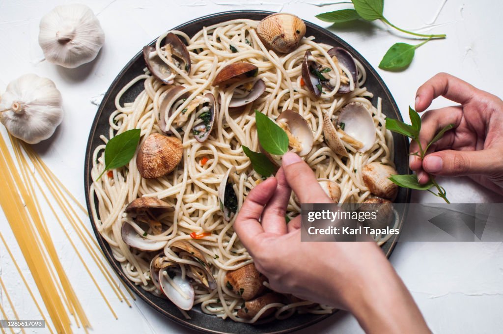 Young woman's hands garnishing Spaghetti Alle Vongole with a basil leaves