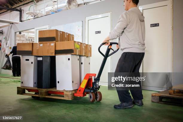 jeune homme poussant le cric de palette dans l’entrepôt de brasserie - diable chariots et charrettes photos et images de collection