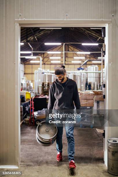 young man carrying aluminum barrel out of brewery distribution warehouse - microbrewery stock pictures, royalty-free photos & images
