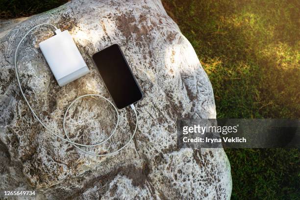 mobile smart phone charging wirelessly by sharing battery via device on a sunny day on a background of rock and green grass. - powerbank fotografías e imágenes de stock