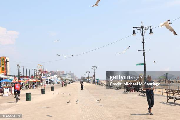 People walk along the Coney Island boardwalk on August 12, 2020 in New York City. New York City is under a heat wave advisory until tonight with many...