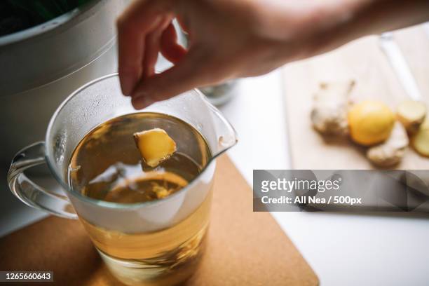 cropped hand of woman adding ginger slice to tea, lleida, spain - ginger stock-fotos und bilder