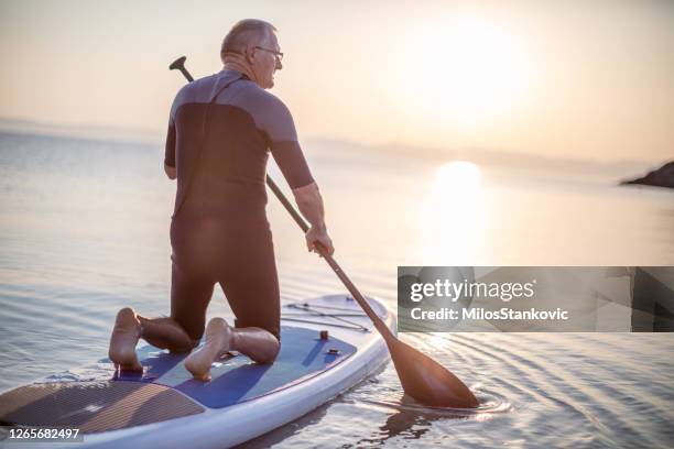 senior man ridding paddle board - paddle board men imagens e fotografias de stock