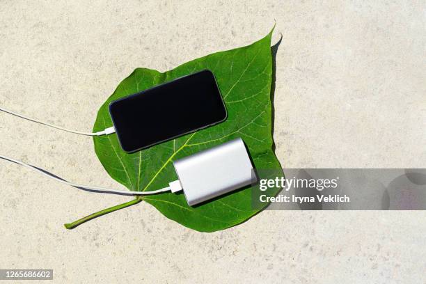 mobile smart phone charging wirelessly by sharing battery via device on a sunny day on a background of green leaf. - powerbank stock-fotos und bilder