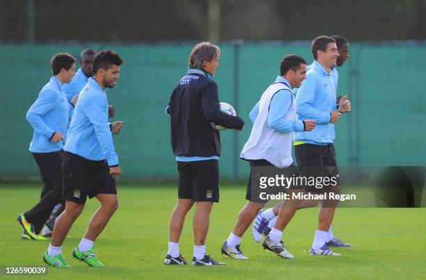 Manager Roberto Mancini looks on as Sergio Aguero, Carlos Tevez and Manchester City players warm up during a training session ahead of their UEFA...