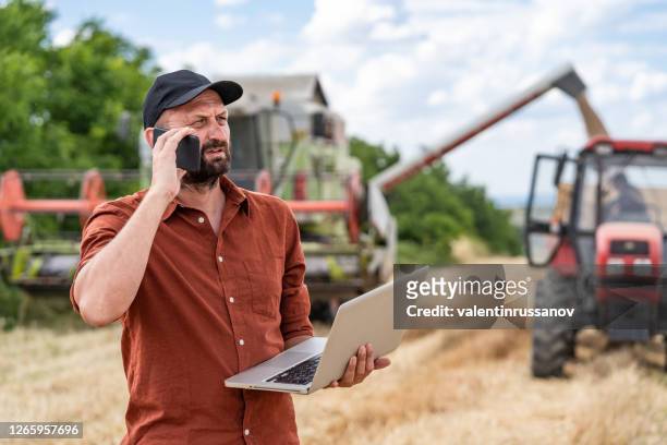 farmer controlled harvest in his field talking on a smart phone and using laptop - farmers insurance stock pictures, royalty-free photos & images