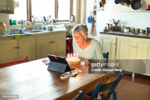 senior grandmother blowing out birthday cake candles on a video call - zoom birthday stock pictures, royalty-free photos & images
