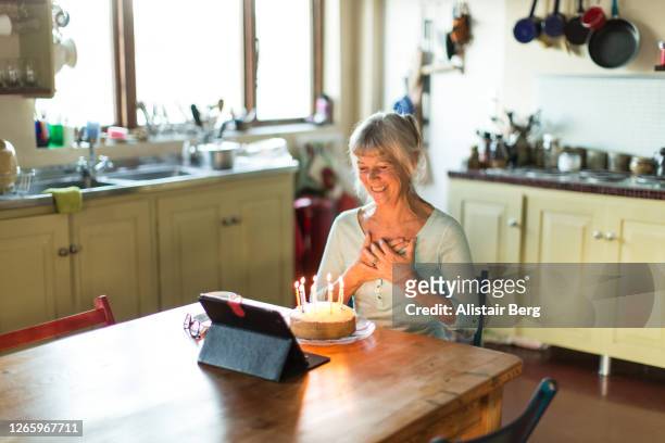 senior grandmother blowing out birthday cake candles on a video call - zoom birthday stock pictures, royalty-free photos & images