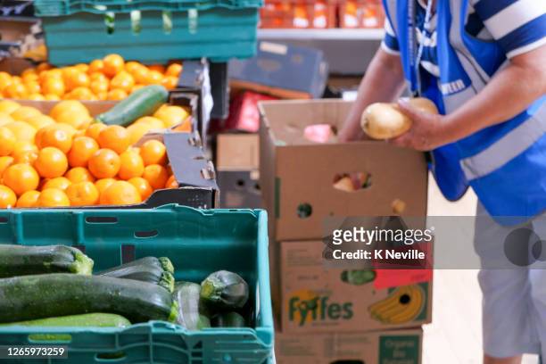 a volunteer worker carefully unpacking fresh vegetables in a food bank distribution centre - foodbanks for the needy stock pictures, royalty-free photos & images