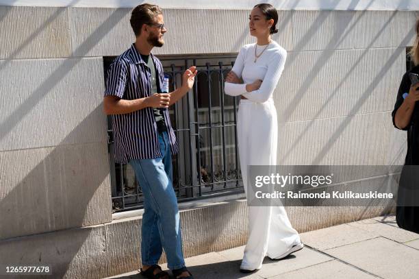 Guests outside MFPEN guy wearing jeans and striped shirt and a girl with white wide pants and white long sleeves top during Copenhagen fashion week...