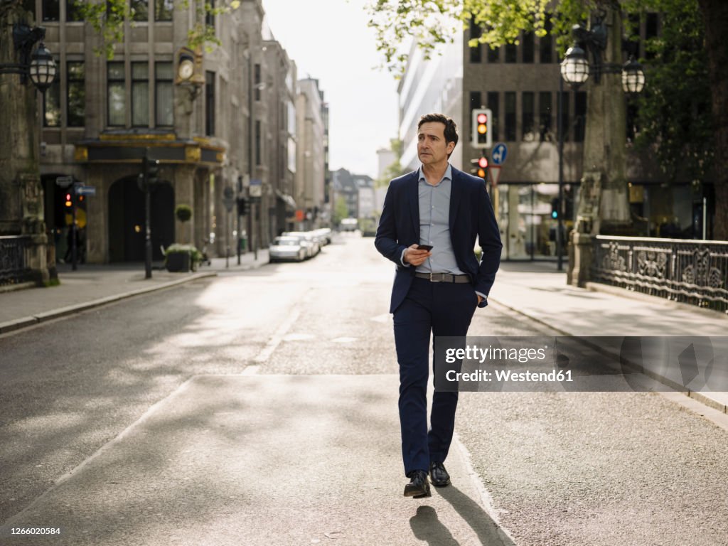 Mature businessman walking on a city street holding smartphone