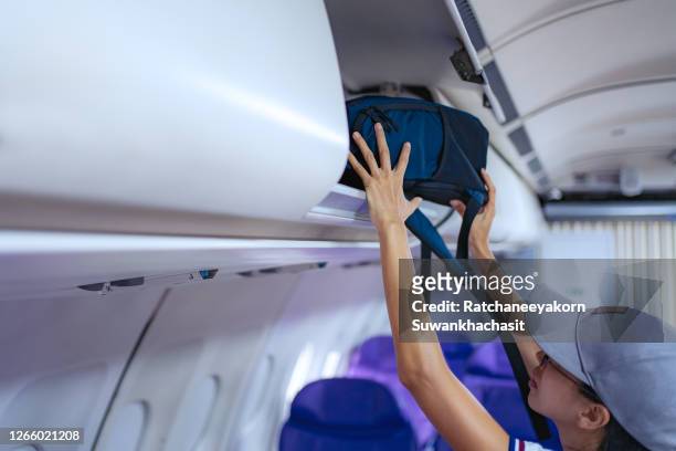 young girl placed her hand luggage into the compartment on the plane. - boarding plane stock-fotos und bilder