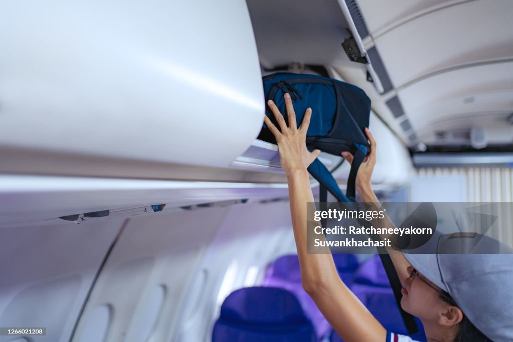 Young girl placed her hand luggage into the compartment on the plane.